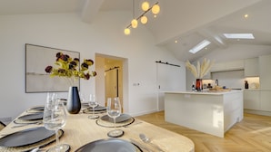 Un espace de repas moderne avec une longue table dressée pour le repas, une cuisine en arrière-plan et une lucarne au-dessus.