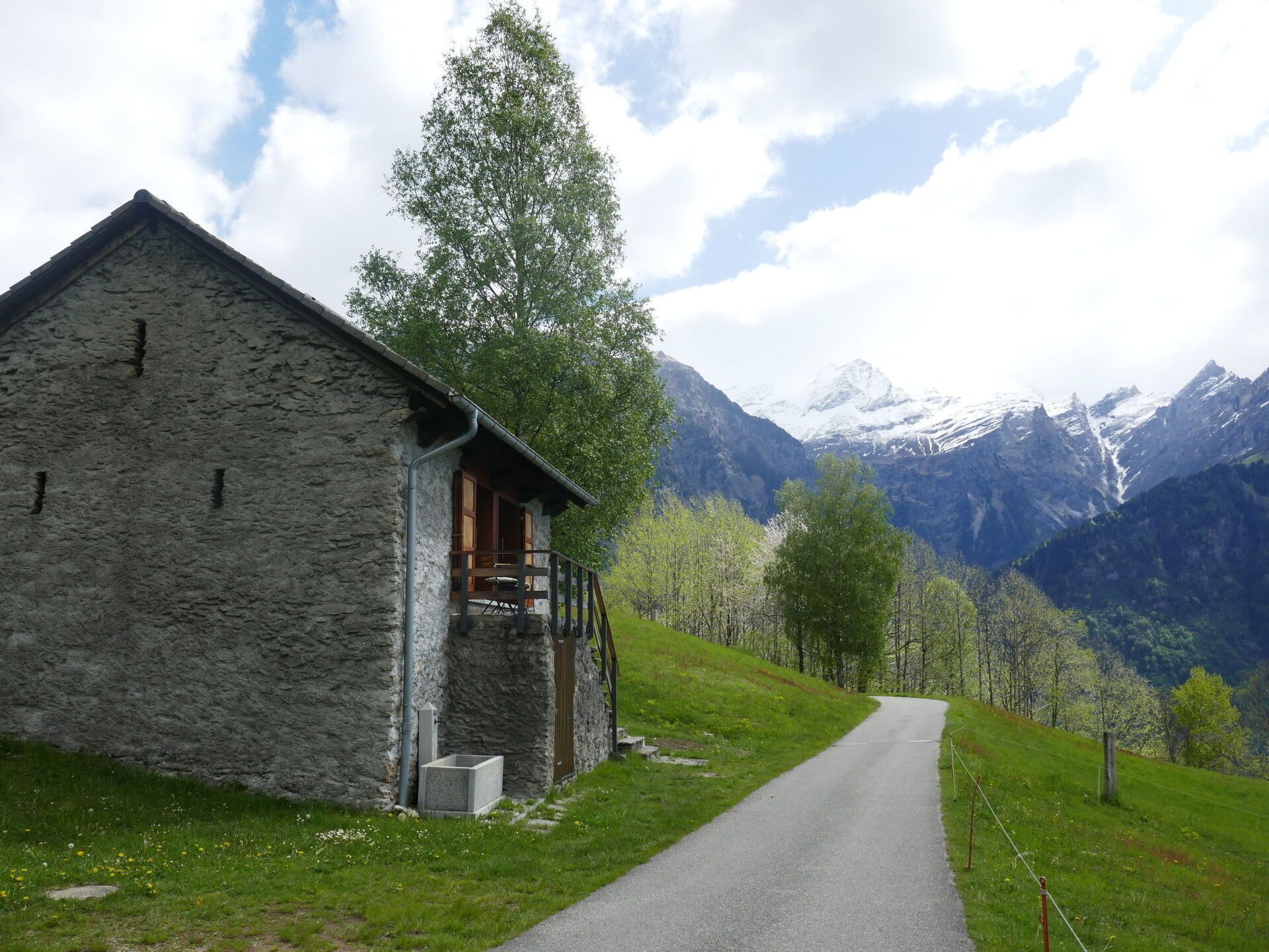 A stone building with a wooden balcony, a paved path, and a mountain backdrop.