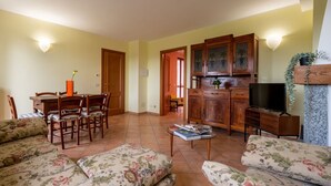 Un salon avec des canapés à motifs floraux, un coin repas avec des chaises et une table en bois, et une cuisine avec des meubles de rangement en bois et un téléviseur.
