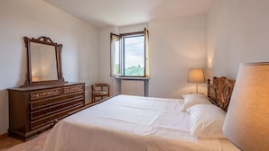 Une chambre à coucher avec un grand lit, une commode, une chaise, une fenêtre et une lampe.