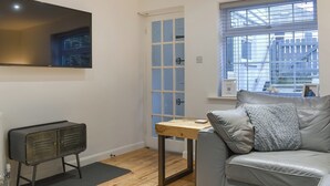 Ein modernes Wohnzimmer mit einem grauen Sofa, einem Holztisch, einem Schrank im Vintage-Stil und einem großen Fenster mit Blick auf die Stadt.