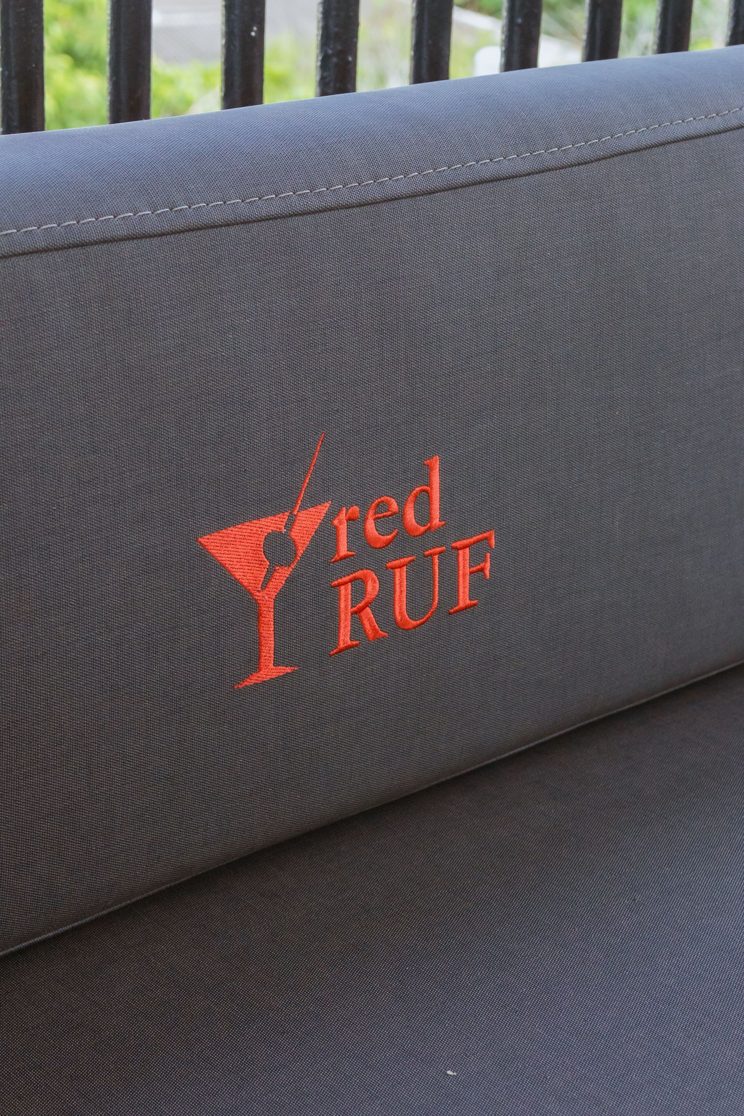 A grey upholstered bench with a logo that reads "red RUF" and a martini glass.