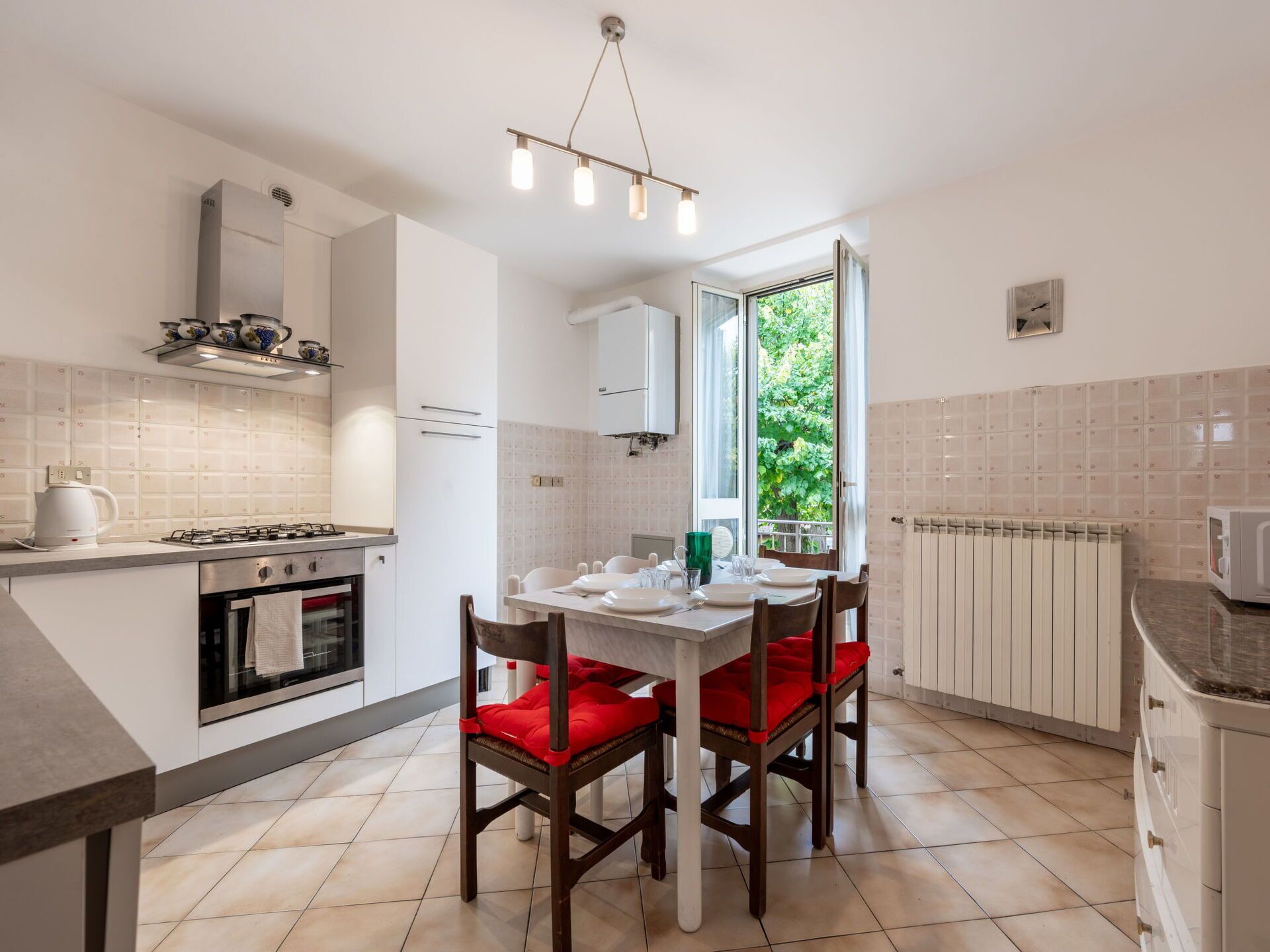 Een moderne keuken met witte kasten, een gasfornuis en een eettafel met rode stoelen.