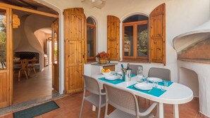 Un comedor con mesa lista para cuatro personas, contraventanas de madera, chimenea y vista al exterior.