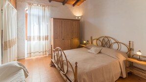 Un dormitorio con techo de madera, una cama con cabecera, un armario y una mesita de noche con una lámpara.