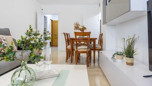 Una sala de estar moderna con comedor, que incluye un sofá, una mesa de centro con un jarrón y vasos, y una mesa de comedor de madera con sillas.