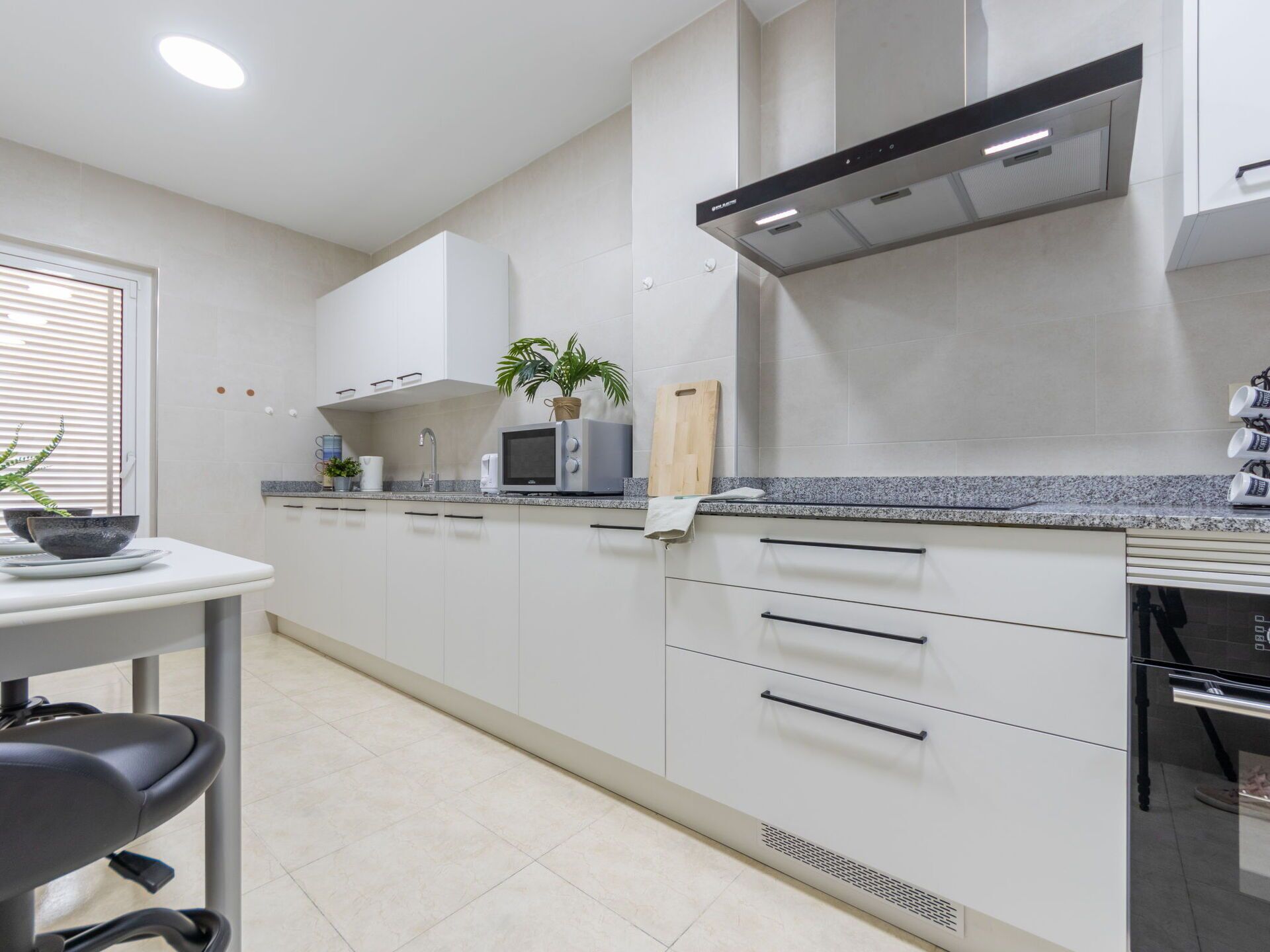 A modern kitchen with white cabinets, a granite countertop, a microwave, and a stainless steel range hood.