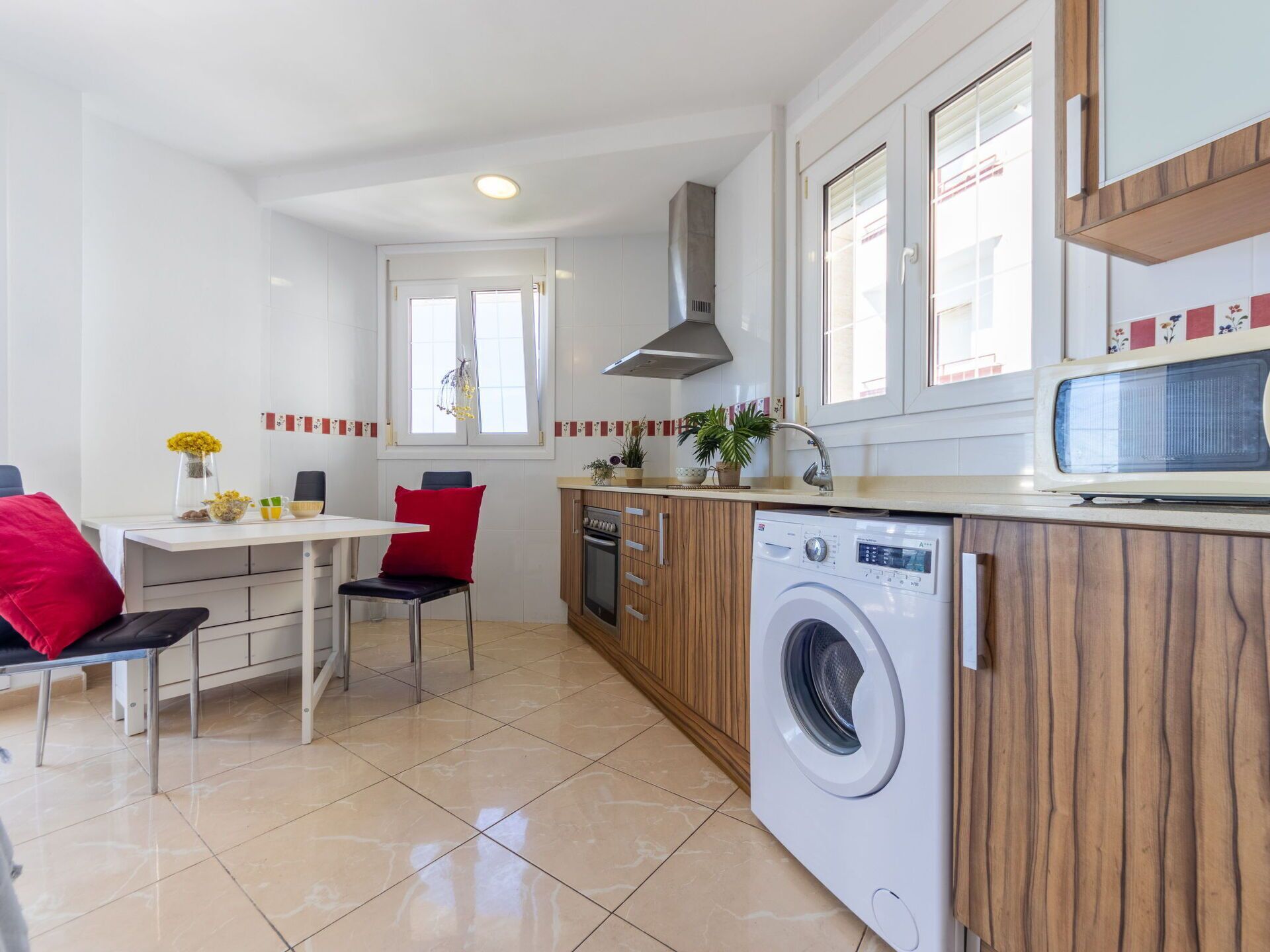 Une cuisine compacte équipée d’un lave-linge, d’un coin repas avec une table et des chaises, et d’une fenêtre avec des rideaux.