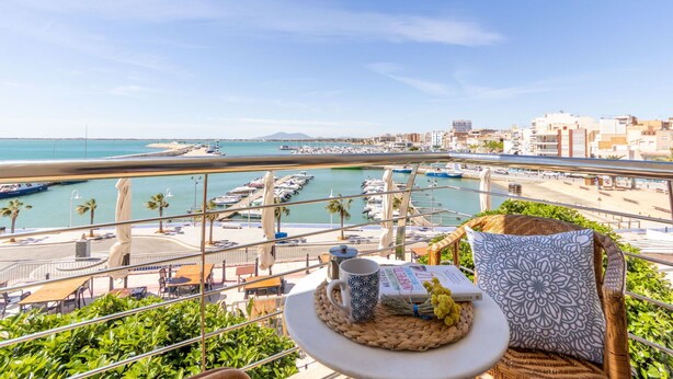 A balcony with a view of a marina, outdoor seating, and a table with a book and a mug.