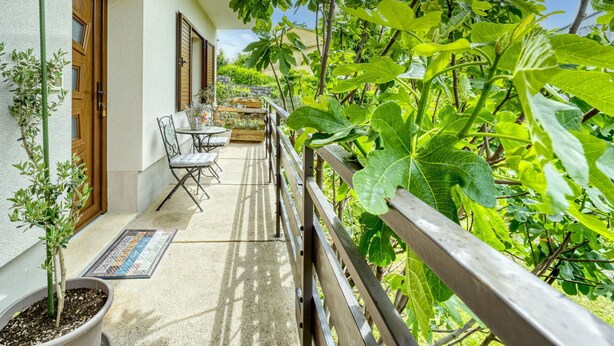A balcony with a table and chairs, surrounded by lush greenery and a wooden railing. - Cosy apartment for 3 guests with A/C, WIFI, TV, patio and panoramic view (Rijeka)
