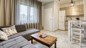 A modern living room with a sofa, a coffee table, and a kitchen area with wooden cabinets and a refrigerator. - Cosy apartment for 3 guests with A/C, WIFI, TV, patio and panoramic view (Rijeka)