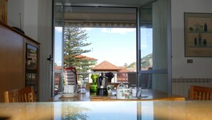 Zona pranzo con tavolo in vetro, sedie e vista su edifici e alberi attraverso una grande finestra.
