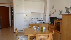 Una cucina compatta con mobili bianchi, un fornello e un'area pranzo con sedie e tavolo in legno.