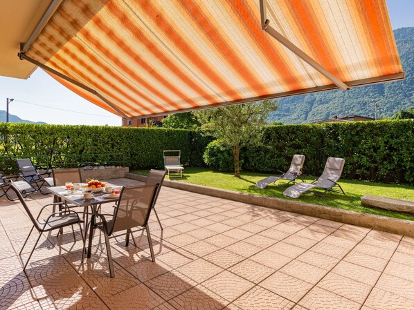 An outdoor patio with a tiled floor, a table with chairs, and a striped awning providing shade.