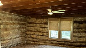 Ein Blockhaus-Interieur mit Holzboden, Steinwänden und Deckenventilator.