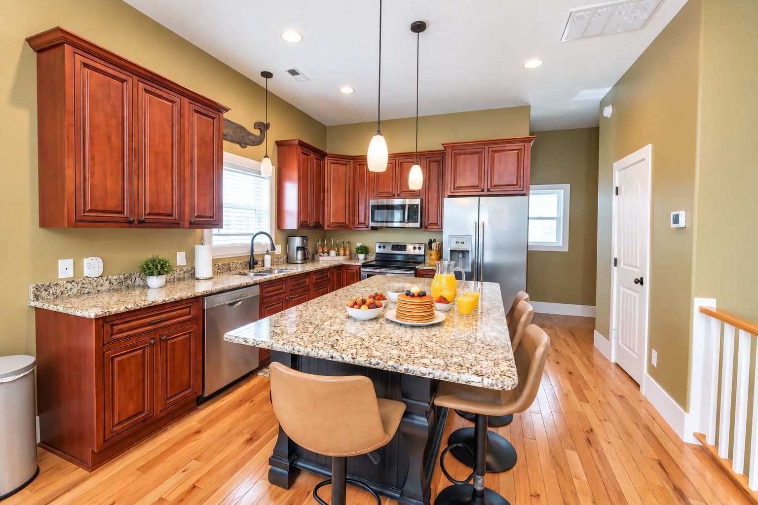 A kitchen with wooden cabinets, granite countertops, stainless steel appliances, and a breakfast bar with seating.