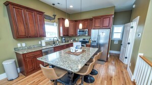 Una cocina con encimeras de granito, armarios de madera y electrodomésticos de acero inoxidable, además de una isla central con taburetes de bar.