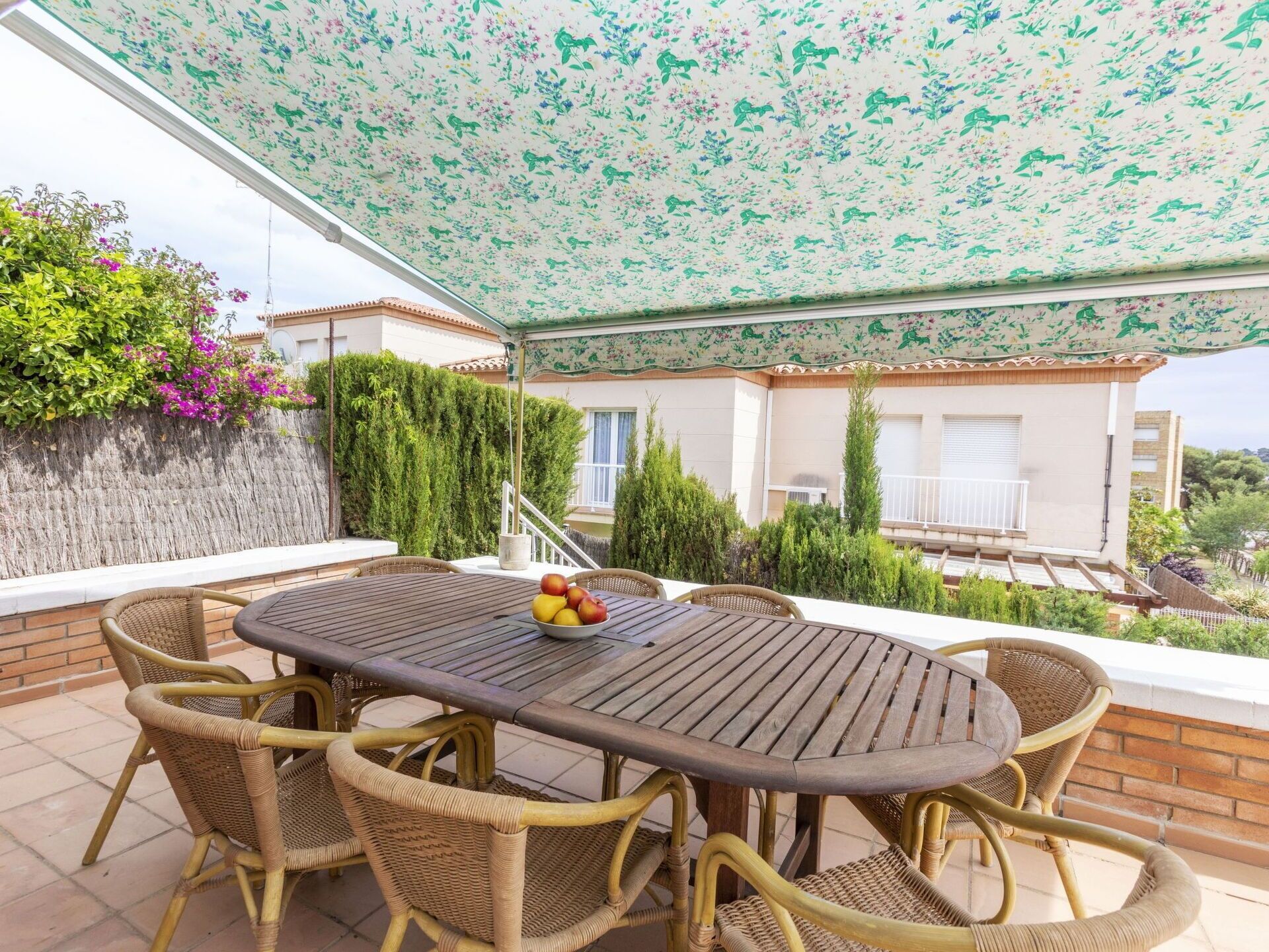 Un espace extérieur abrité, aménagé pour les repas, avec des meubles en osier et une table dressée avec des fruits.