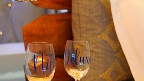 A room with a bed, a wooden headboard, and two wine glasses on a wooden table. - Nili Deluxe (Sarandë)
