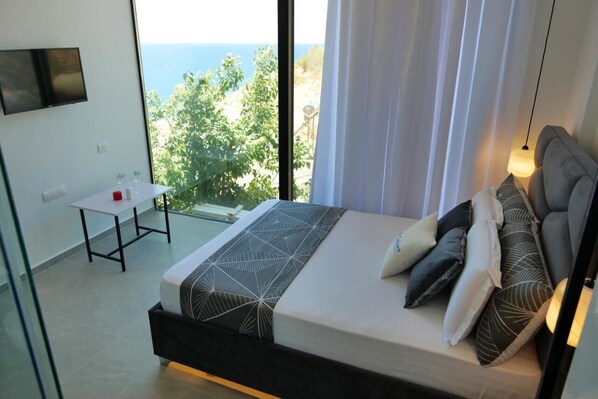 A modern bedroom with a large bed, a small table, and a TV mounted on the wall. - Nili Deluxe (Sarandë)