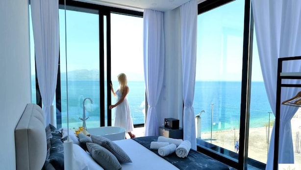 A modern bedroom with a large bed, a bathtub, and a view of the sea. - Nili Deluxe (Sarandë)