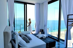 A modern bedroom with a large bed, a bathtub, and a view of the sea. - Nili Deluxe (Sarandë)