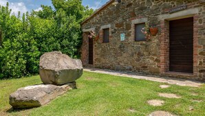 Un edificio de piedra con una pared de piedra rústica, una gran roca en primer plano y una zona cubierta de hierba.