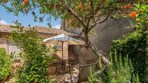 A patio with a table and chairs, surrounded by greenery and a stone wall. - Lovely apartment in villa with A/C, WIFI, pool, TV, patio, pets allowed and panoramic view (Cinigiano)