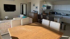 Een moderne keuken met witte kasten, een magnetron en een spoelbak. Er is een eethoek met een houten tafel en stoelen.