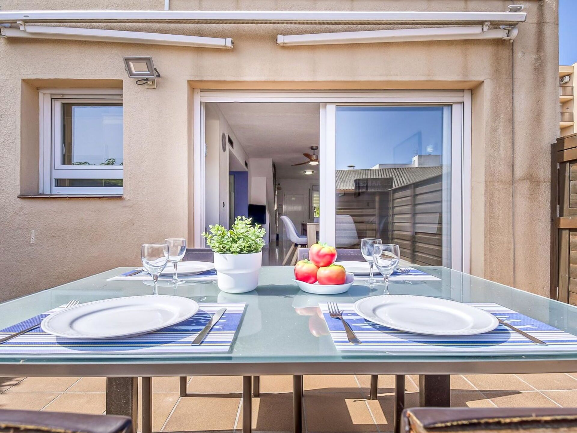 Un área de comedor al aire libre con una mesa de vidrio, dos sillas y una planta en maceta.
