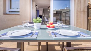 Un área de comedor al aire libre con una mesa de vidrio, dos sillas y una planta en maceta.