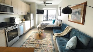 A modern kitchen with a dining area, a sofa, and a bed in a bright room with a view.