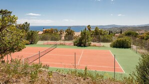 A tennis court with a net, surrounded by trees and a view of the sea and distant hills. - Nice apartment for 2 guests with pool, WIFI, TV and balcony (Roquebrune-sur-argens)
