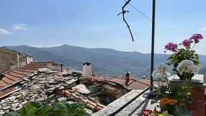 A stone-paved terrace with a view of distant mountains, a stone wall, and potted plants.
