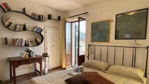 A bedroom with a bed, bedside table, bookshelves, a desk, a window, and a painting.