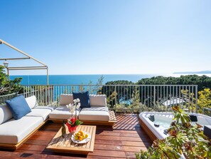 Une terrasse en bois avec un canapé, un jacuzzi et une table sur laquelle sont disposés des fruits et une bouteille.