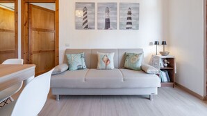 Un salon moderne avec un canapé gris, une porte en bois et trois tableaux représentant des phares accrochés au mur.