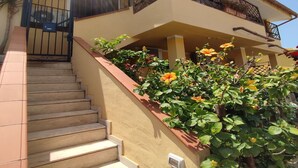 Un bâtiment à deux étages, avec un escalier menant à un balcon agrémenté de plantes et de fleurs en pot.