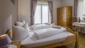 A bedroom with two single beds, a wooden wardrobe, a table with a bottle and glass, and a window with curtains. - Beautiful private villa for 22 guests with WIFI, TV, patio and pets allowed (Fügen)