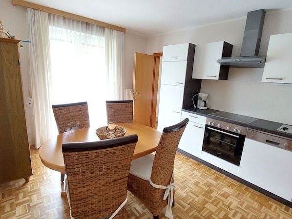 Een compacte keuken met een eethoek, met een ronde tafel, rieten stoelen, een ingebouwde oven en een koffiezetapparaat.