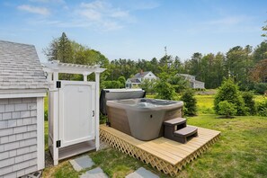 A hot tub with a wooden deck and steps, a white pergola, and a house in the background.