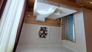 A room with a wooden ceiling, a bed with white linens, a window, and a wall-mounted abstract painting.