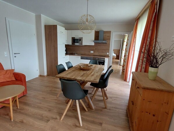 Une cuisine moderne avec des meubles blancs, une table à manger en bois et des chaises noires.