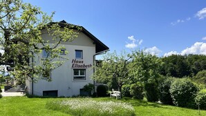 Ein Gebäude namens 'Haus Elisabeth' mit weißer Fassade, einer sichtbaren Treppe und einem Garten mit weißen Blumen.