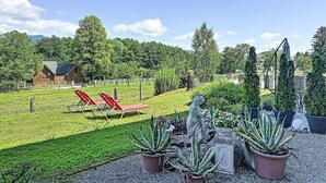 Eine Terrassenanlage mit roten Liegestühlen, Topfpflanzen und einer Statue.