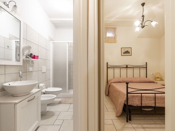 A bathroom with a sink, toilet, and shower. There is a bed with a metal frame and a headboard.