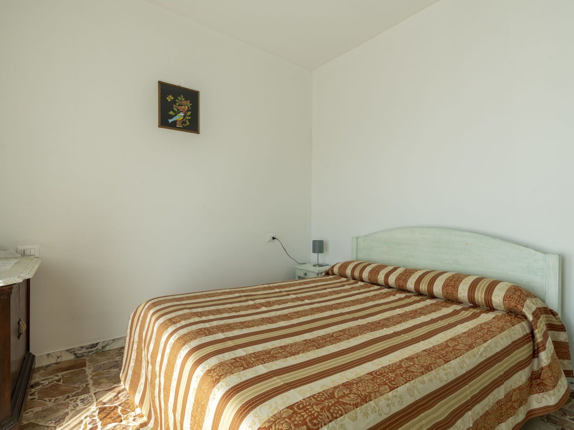 A bedroom with a bed, a nightstand, a lamp, and a wall-mounted picture.
