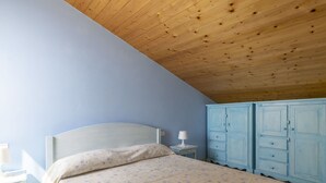 A bedroom with a wooden ceiling, a bed with floral bedding, a nightstand with a lamp, and a blue wardrobe. - Cosy apartment for 4 guests with A/C, WIFI, balcony and panoramic view (Terzorio)