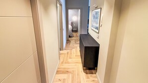 A hallway with a wooden herringbone floor, a black bench, and a framed picture on the wall.