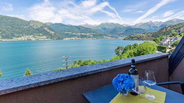 A balcony with a table set for two, overlooking a lake with mountains in the background.